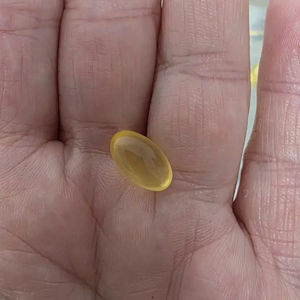 a hand holding a yellow hoki fish oil capsule pill